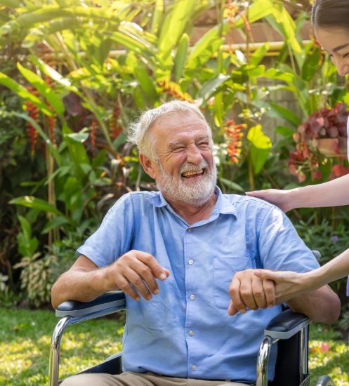 happy-nurse-holding-laughing-elderly-man-hand-wheelchair-garden-nursing-home